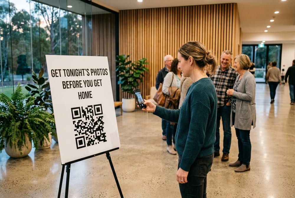 A printed sign on an easel in a church foyer reads Get tonight’s photos before you get home above a large QR code. A woman holds her phone up to scan it while a few people wait and talk behind her.